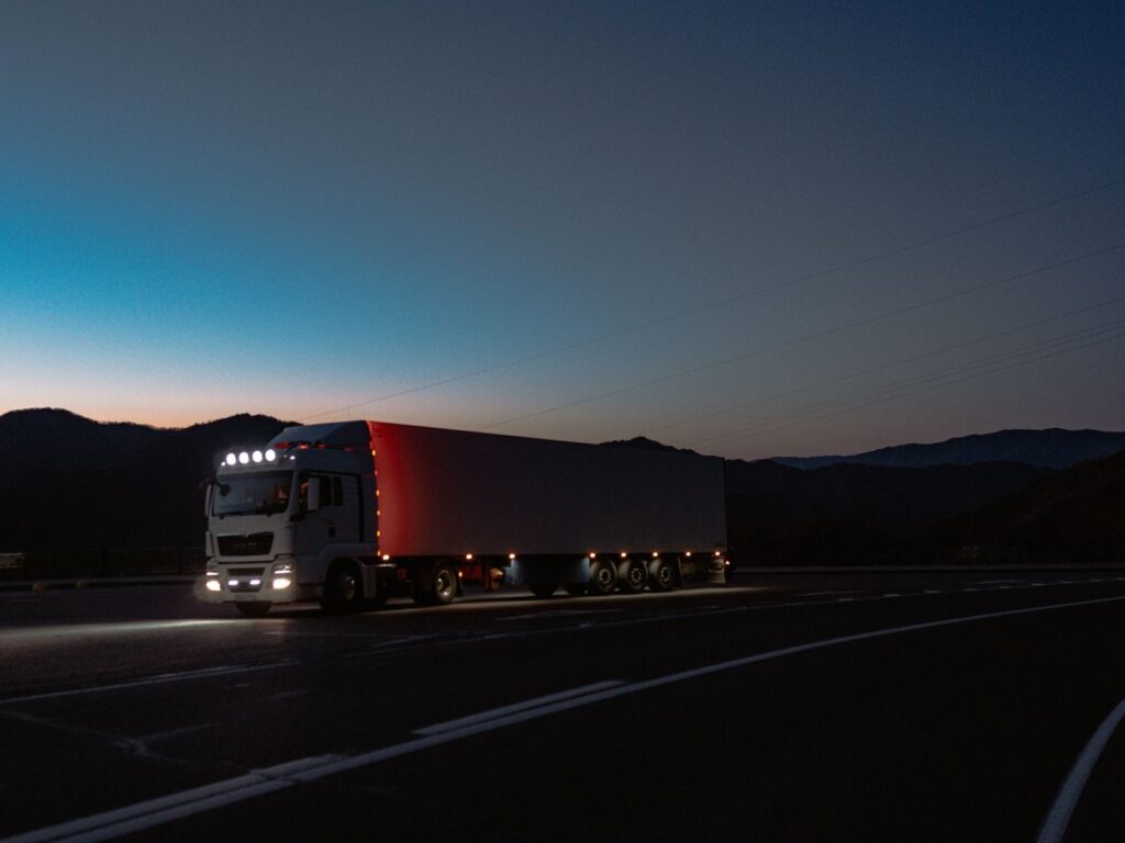 Large cargo truck travels on Altai road at night with mountains silhouetted against twilight sky.